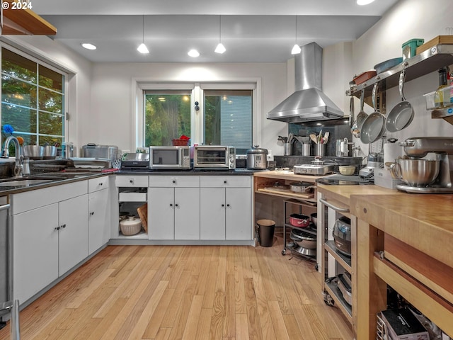 kitchen with dark countertops, wall chimney range hood, a sink, stainless steel microwave, and white cabinetry