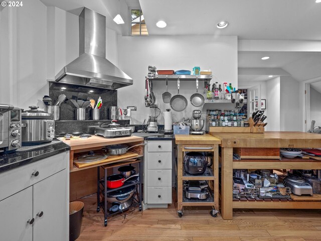 kitchen featuring wall chimney range hood, white cabinets, tasteful backsplash, light hardwood / wood-style flooring, and butcher block counters