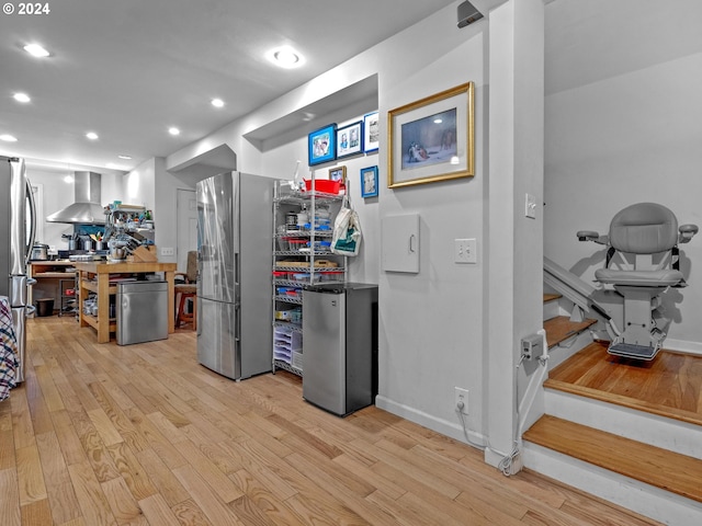 kitchen featuring wall chimney range hood, stainless steel fridge, and light hardwood / wood-style floors