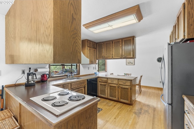 kitchen featuring sink, black dishwasher, light wood-type flooring, kitchen peninsula, and stainless steel fridge