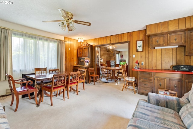 carpeted dining space with a textured ceiling, wooden walls, and ceiling fan