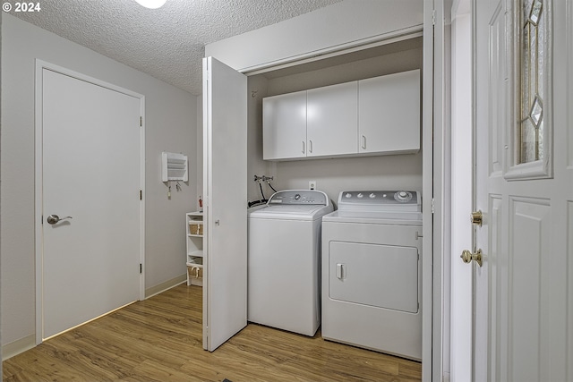 clothes washing area with washing machine and clothes dryer, cabinets, a textured ceiling, and light wood-type flooring