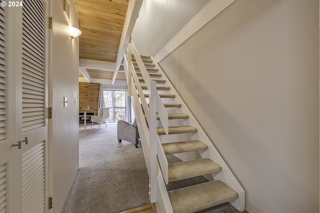 stairway featuring beamed ceiling, wooden ceiling, and carpet