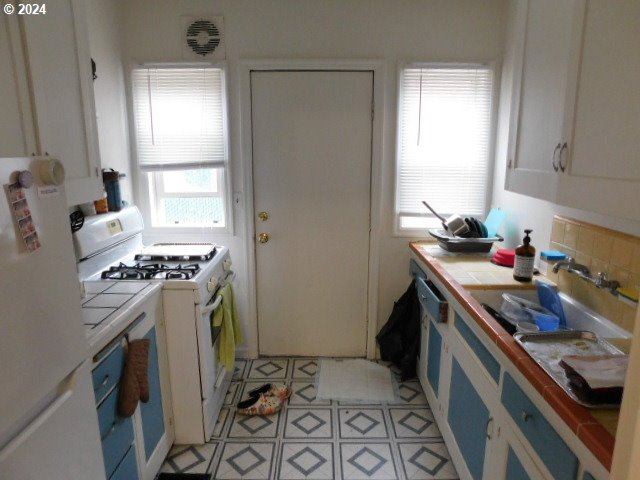 kitchen featuring a healthy amount of sunlight, tile counters, white appliances, and white cabinetry