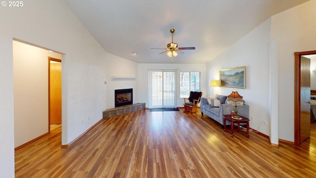 living room featuring ceiling fan, high vaulted ceiling, a tiled fireplace, and light hardwood / wood-style floors