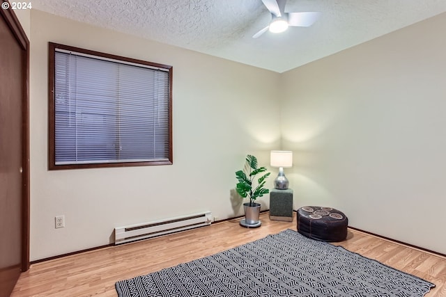 living area with ceiling fan, light wood-type flooring, a textured ceiling, and a baseboard heating unit