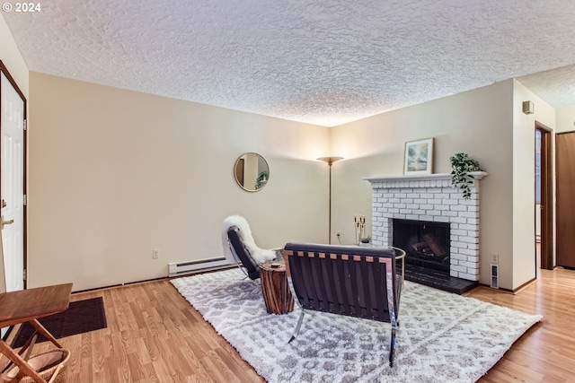 living room featuring light wood-type flooring, a textured ceiling, a brick fireplace, and a baseboard heating unit