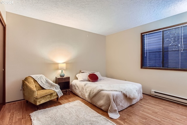 bedroom with light hardwood / wood-style floors, a textured ceiling, and a baseboard radiator