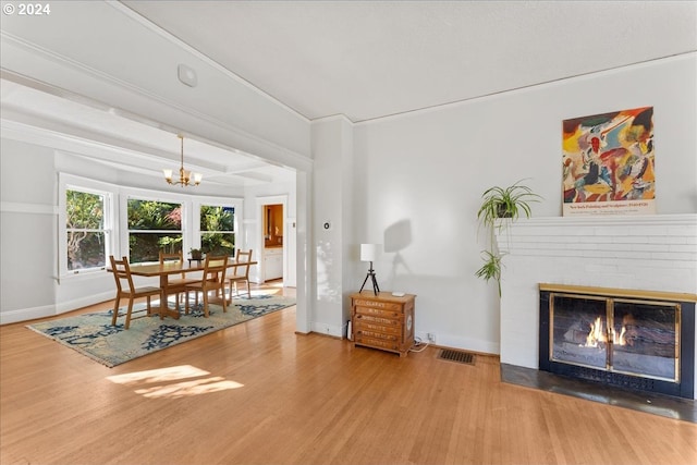 unfurnished dining area with hardwood / wood-style flooring, an inviting chandelier, ornamental molding, and a brick fireplace