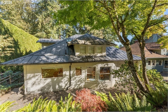 rear view of property with metal roof, glass enclosure, and a standing seam roof