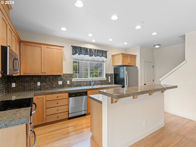 kitchen with a kitchen bar, stainless steel appliances, light hardwood / wood-style floors, a center island, and sink