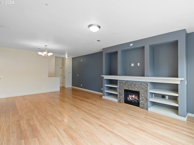 unfurnished living room featuring a fireplace, light wood-type flooring, and a notable chandelier