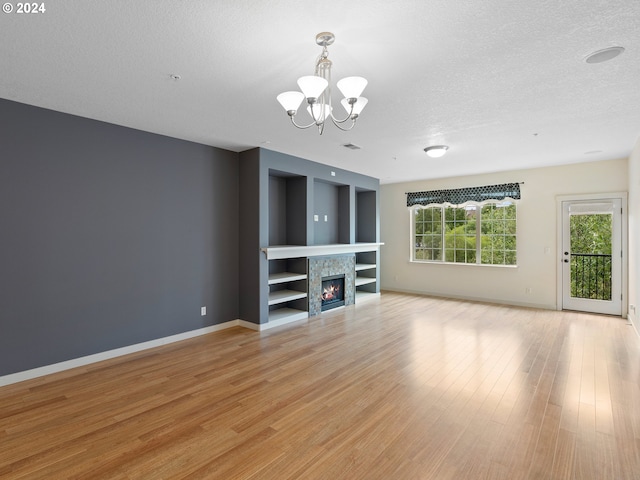 unfurnished living room featuring a chandelier, a textured ceiling, and light hardwood / wood-style flooring