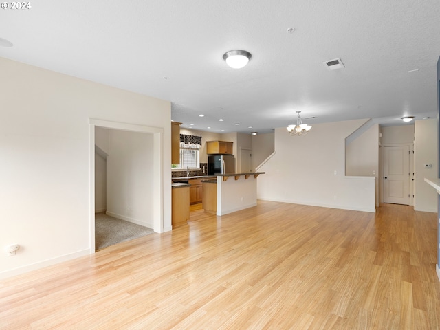 unfurnished living room with light wood-type flooring, sink, a notable chandelier, and a textured ceiling