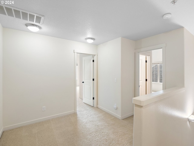 empty room with light colored carpet and a textured ceiling