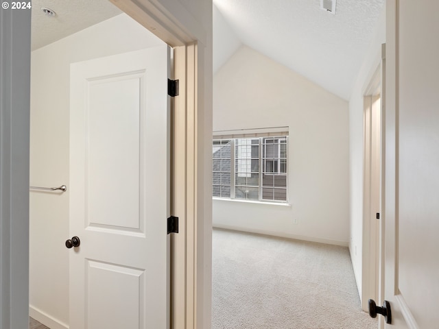 hallway with a textured ceiling, vaulted ceiling, and carpet