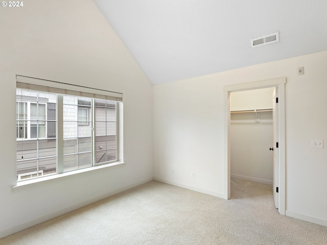 unfurnished bedroom with lofted ceiling, light carpet, a closet, and a walk in closet