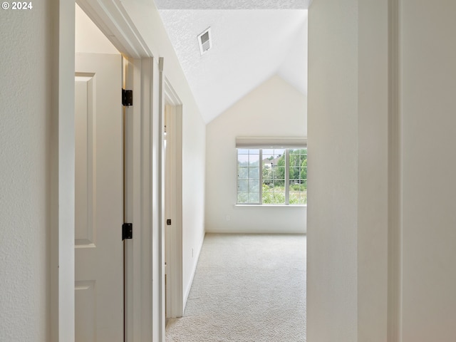 hallway featuring a textured ceiling, light carpet, and vaulted ceiling