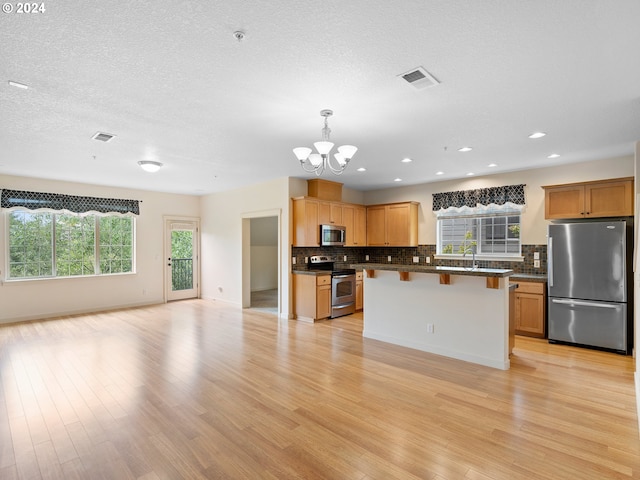 kitchen featuring light hardwood / wood-style floors, an inviting chandelier, a kitchen island, appliances with stainless steel finishes, and decorative light fixtures