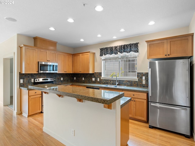 kitchen featuring a kitchen bar, a center island, sink, light wood-type flooring, and appliances with stainless steel finishes