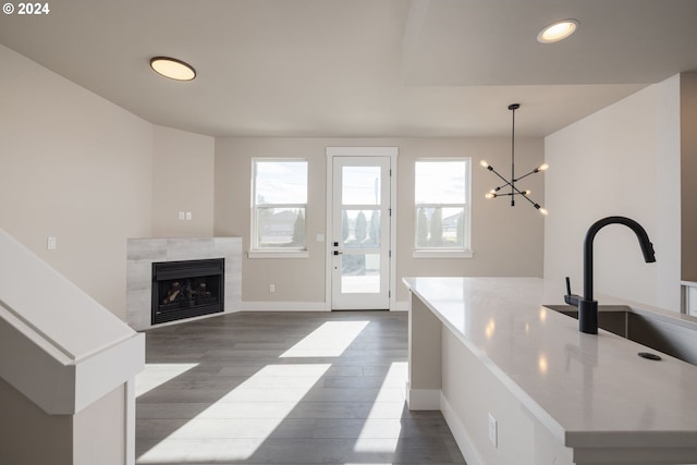 kitchen featuring a tiled fireplace, sink, hanging light fixtures, a notable chandelier, and dark hardwood / wood-style flooring