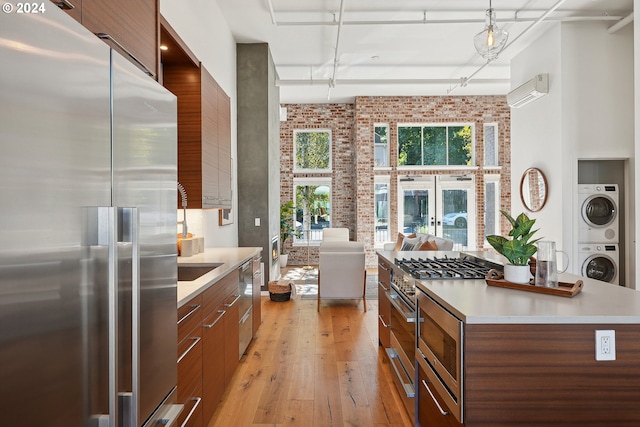 kitchen with light hardwood / wood-style floors, stacked washer / drying machine, hanging light fixtures, brick wall, and high quality appliances