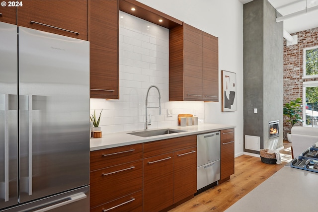 kitchen featuring sink, stainless steel appliances, a fireplace, light hardwood / wood-style floors, and decorative backsplash