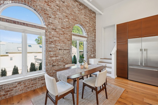 dining room with light wood-type flooring, a wealth of natural light, and brick wall