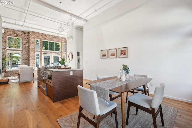 dining room featuring wood-type flooring, a towering ceiling, and brick wall