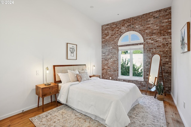 bedroom with a high ceiling, light hardwood / wood-style flooring, and brick wall