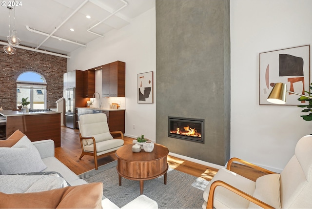 living room with wood-type flooring, sink, a fireplace, a high ceiling, and brick wall