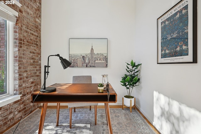 office with brick wall, hardwood / wood-style floors, and plenty of natural light