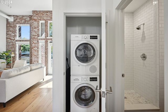 clothes washing area featuring light wood-type flooring, stacked washer and clothes dryer, and brick wall