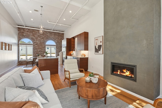 living room with brick wall, a towering ceiling, light hardwood / wood-style floors, and a large fireplace