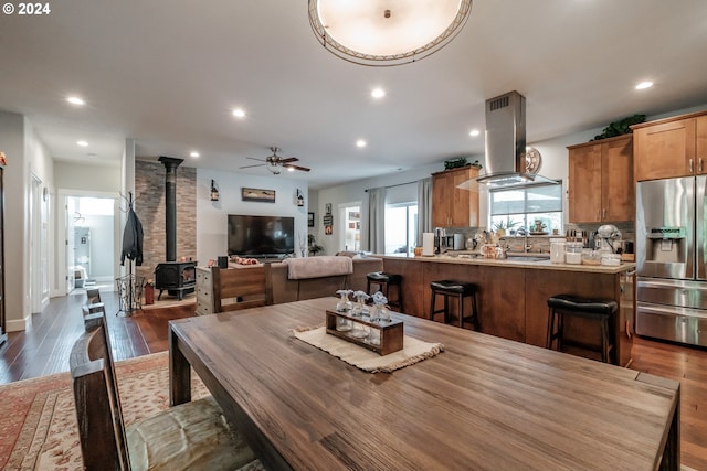 dining space with a wood stove, dark wood-type flooring, and ceiling fan