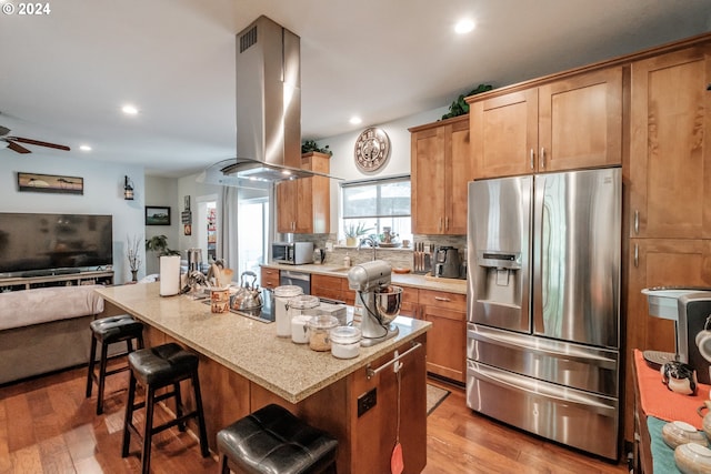 kitchen featuring appliances with stainless steel finishes, light hardwood / wood-style floors, island exhaust hood, a breakfast bar, and ceiling fan