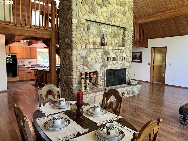 dining room featuring beamed ceiling, dark wood-type flooring, high vaulted ceiling, a stone fireplace, and wooden ceiling