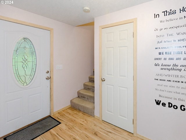 entryway with light wood-style floors, a textured ceiling, baseboards, and stairs