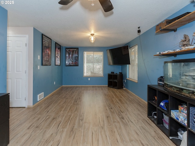 unfurnished living room with a textured ceiling, wood finished floors, visible vents, and baseboards