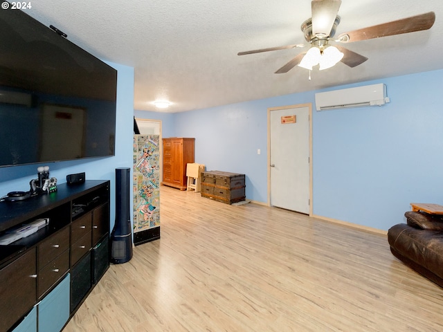 living room featuring a textured ceiling, an AC wall unit, baseboards, and light wood-style floors