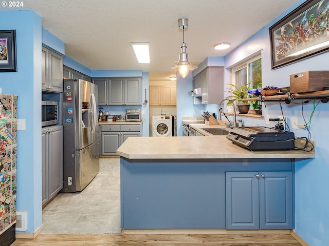 kitchen featuring gray cabinets, appliances with stainless steel finishes, a sink, independent washer and dryer, and a peninsula