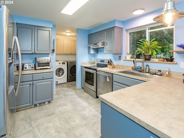 kitchen with under cabinet range hood, a sink, appliances with stainless steel finishes, gray cabinets, and washing machine and clothes dryer