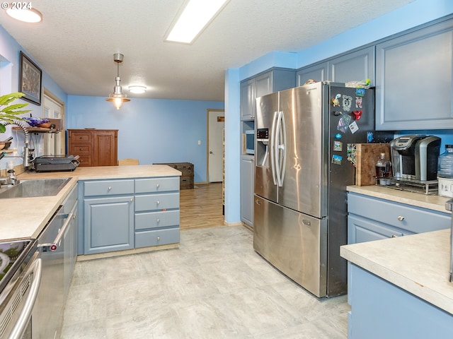 kitchen featuring a peninsula, blue cabinets, stainless steel appliances, light countertops, and a sink