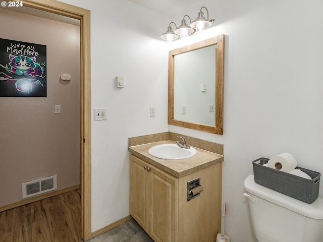 half bath featuring visible vents, toilet, vanity, wood finished floors, and baseboards