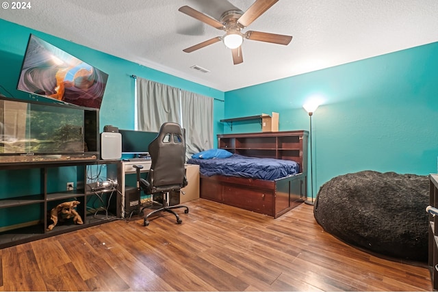 bedroom featuring a ceiling fan, visible vents, a textured ceiling, and wood finished floors