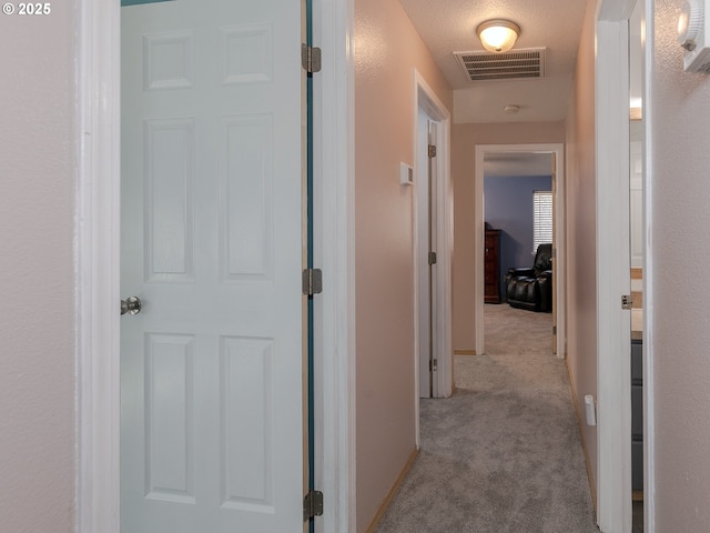 hall with carpet, visible vents, and baseboards