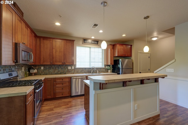 kitchen with stainless steel appliances, a sink, dark wood finished floors, visible vents, and backsplash