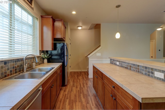 kitchen featuring a sink, light wood-type flooring, backsplash, brown cabinetry, and dishwasher
