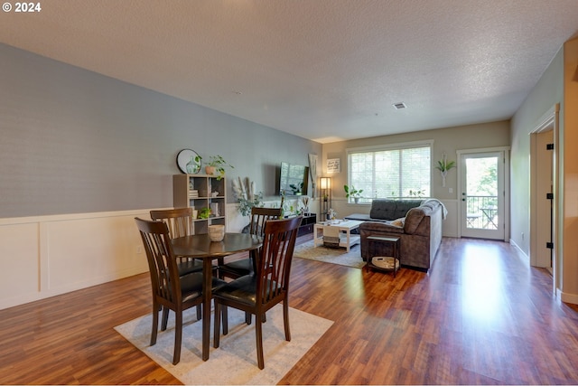 dining space featuring wainscoting, wood finished floors, visible vents, and a textured ceiling