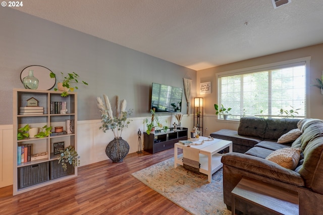 living area with wood finished floors, a textured ceiling, and wainscoting